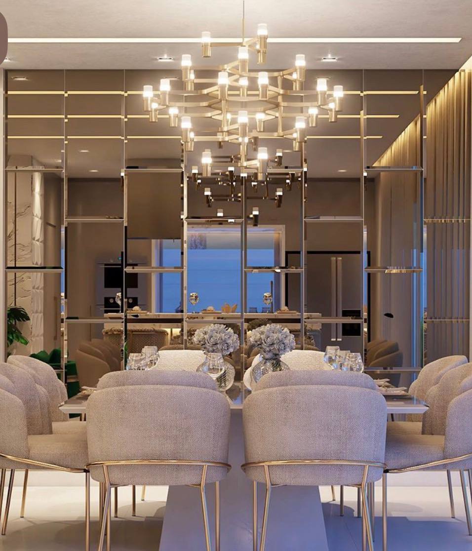 Comedor de lujo con muro espejado en bronce con despiece geométrico y gran lámpara dorada de brazos